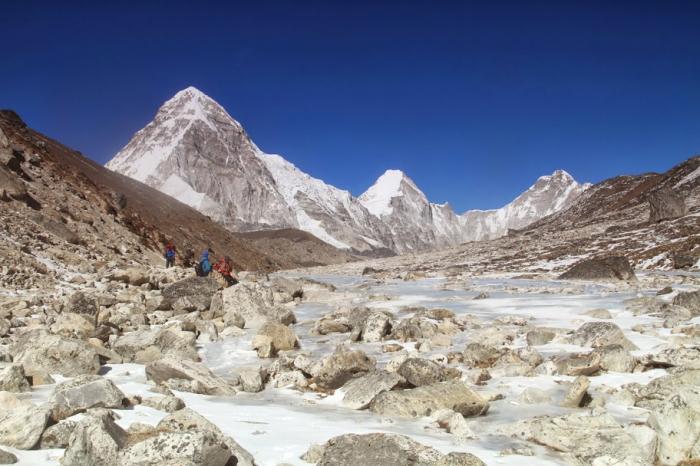 Trekkers walking the rocky glacier moraine on the upper Khumbu trail, snow peaks behind, on the way to Everest Base Camp.