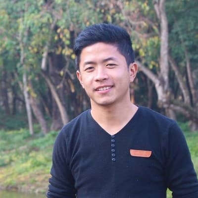 Arjun Gurung smiling, in a black sweater, with trees and grass behind him.