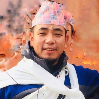 Dil Bahadur Gurung smiling, in a patterned cloth cap, a blue and gray jacket and a white scarf over his shoulders, against a blurred orange background.